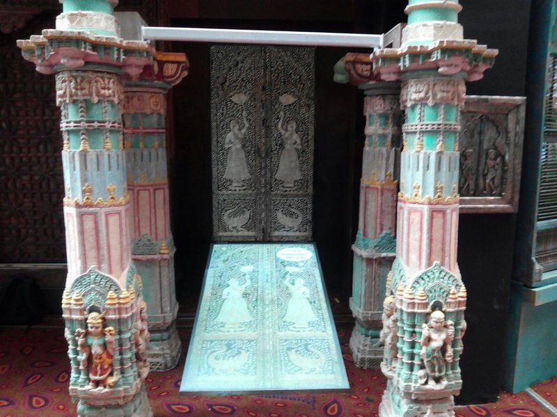 A lit glass floor panel between two carved pillars, with a carved door behind